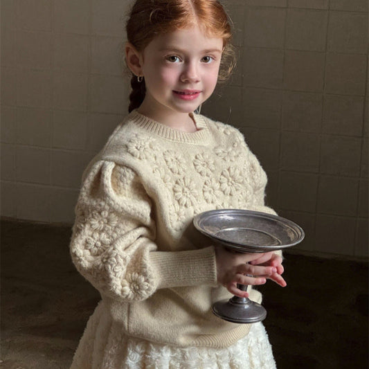 Young girl in a cream sweater holding a silver dish against a neutral background