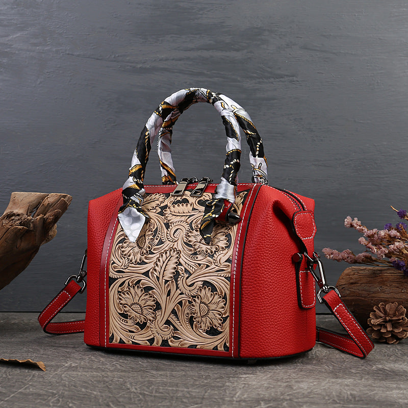 Red handbag with intricate design and patterned handle on a dark surface