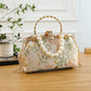 Decorative handbag with floral pattern and pearl embellishments on a wooden surface.