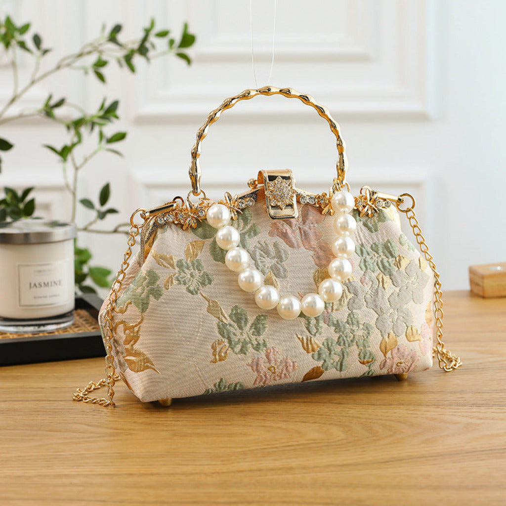 Decorative handbag with floral pattern and pearl embellishments on a wooden surface.