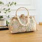 Decorative handbag with floral pattern and pearl embellishments on a wooden surface.