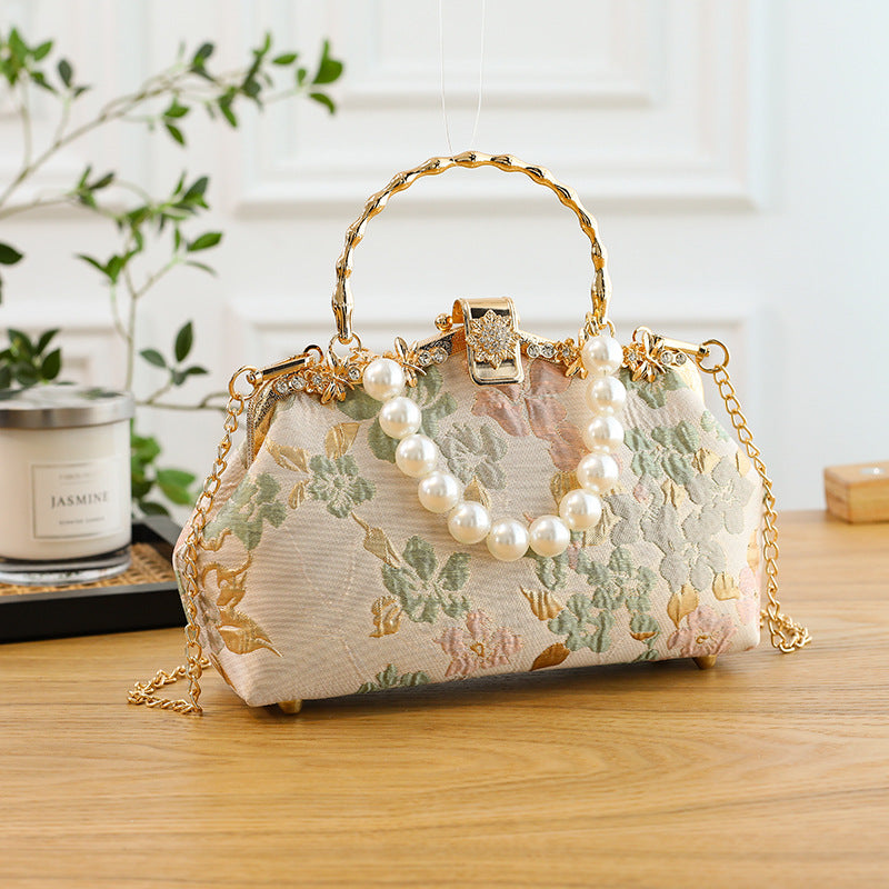 Decorative handbag with floral pattern and pearl embellishments on a wooden surface.