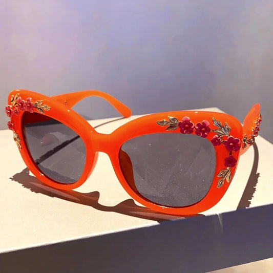 Orange sunglasses with floral embellishments on a reflective surface