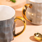 Two ceramic mugs with gold handles on a beige surface.