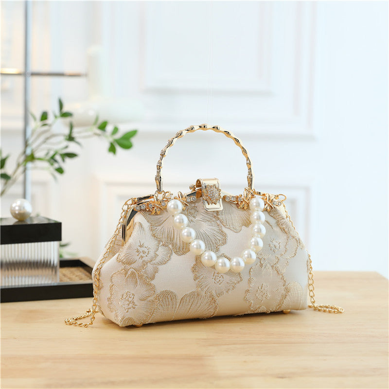 Elegant handbag with floral lace design and pearl embellishments on a wooden surface.