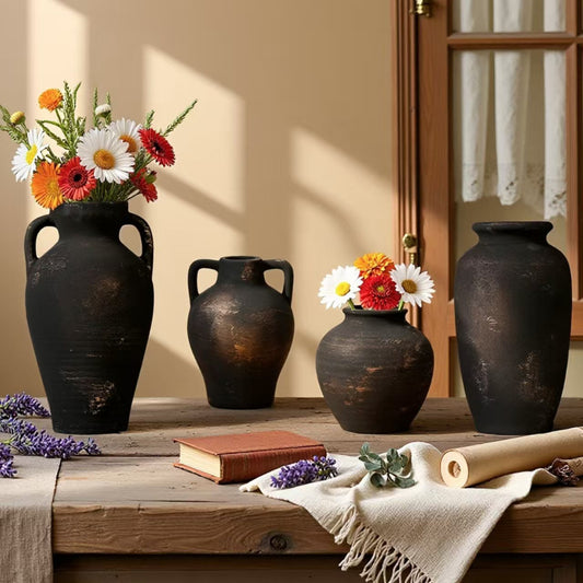 Four black earthenware vases with flowers on a wooden surface.