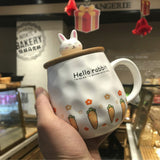 White mug with 'Hello rabbit' design held in front of a bakery counter.