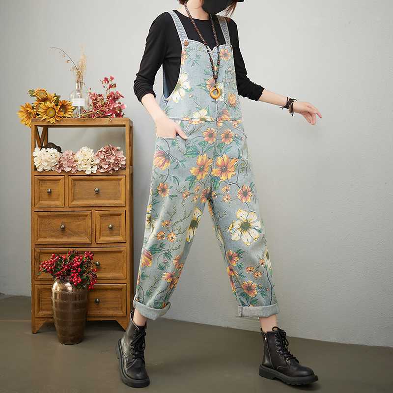 Person wearing floral overalls standing in a room with wooden furniture and flowers.