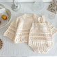 Knitted baby outfit with top and overalls on a textured surface