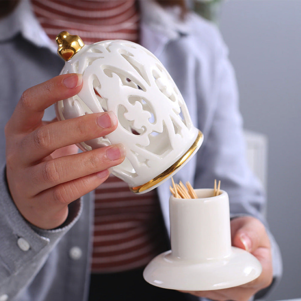 Person holding a decorative white and gold toothpick holder with intricate designs.