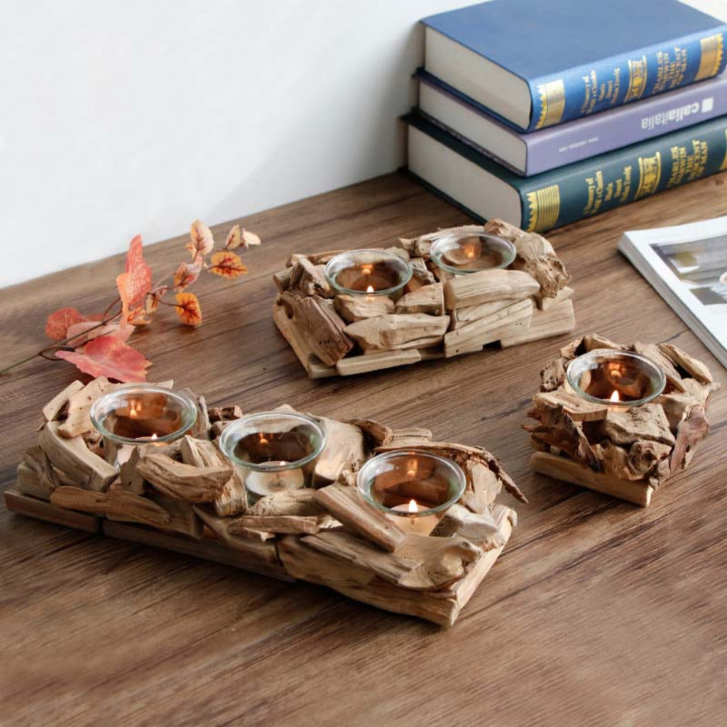 Driftwood candle holders with candles on a wooden surface, books in the background