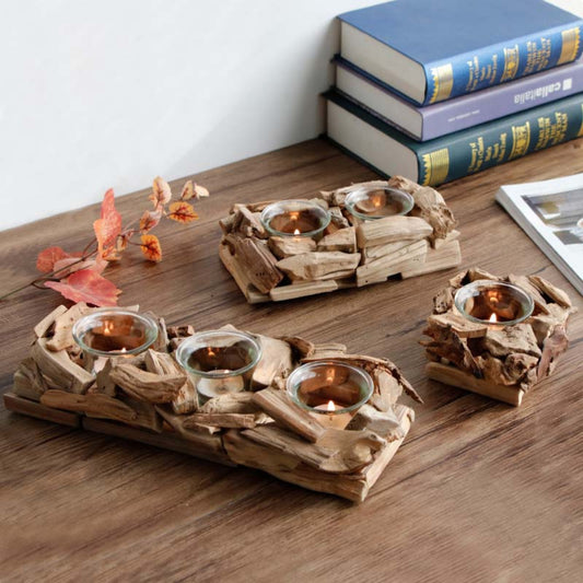 Driftwood candle holders with candles on a wooden surface, books in the background