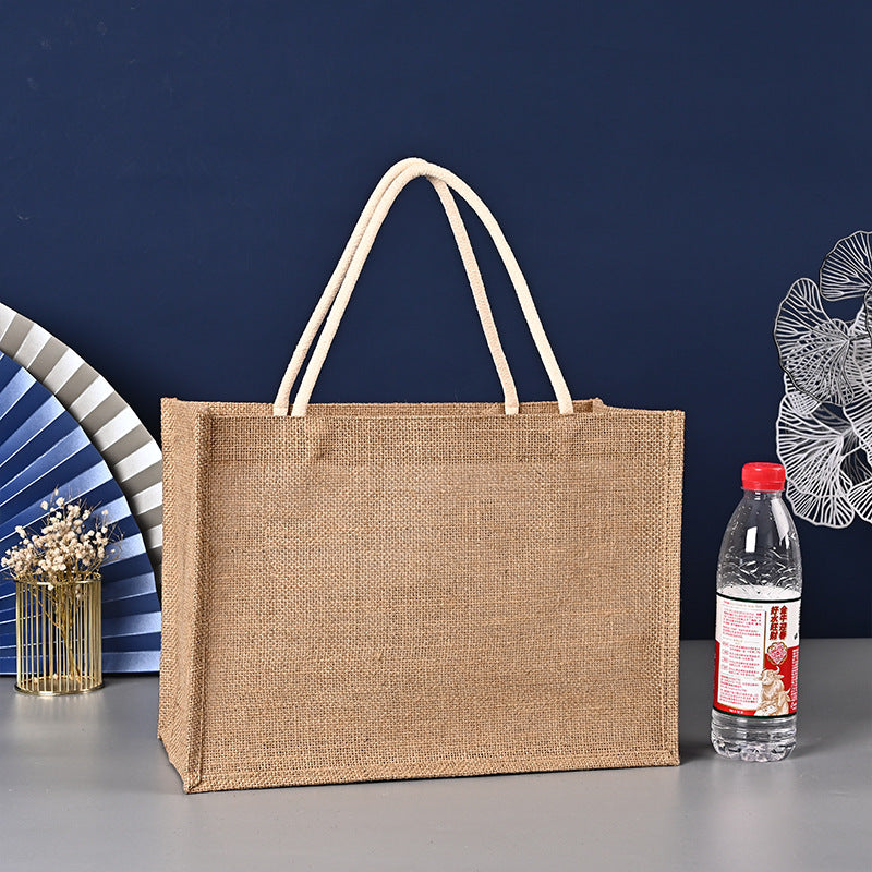 Brown jute bag with white handles on a gray surface against a blue wall.