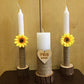 Three candles with sunflower decorations and a heart-shaped plaque on a wooden surface.