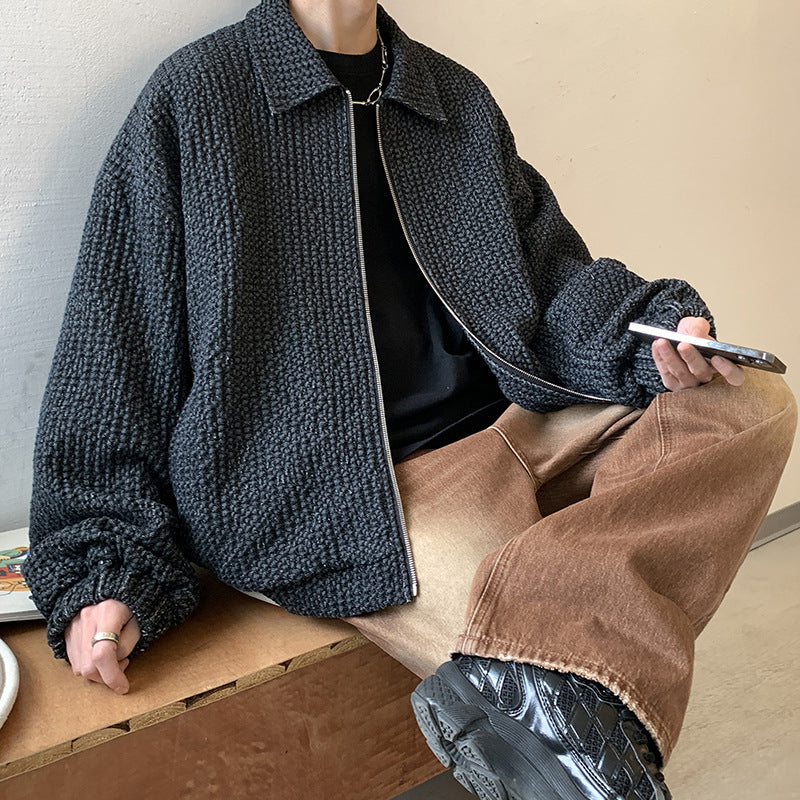 Person wearing a dark textured jacket and brown pants sitting on a wooden bench.