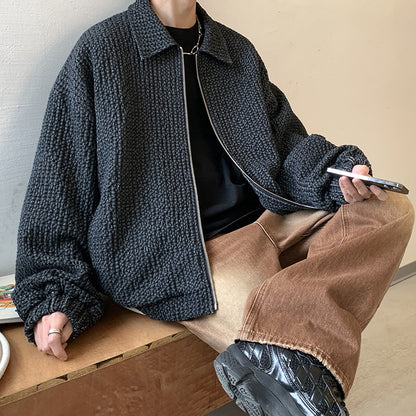 Person wearing a dark textured jacket and brown pants sitting on a wooden bench.