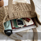 Knitted beige bag with books and a phone inside on a light surface