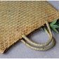 Woven straw bag with handles on a textured surface with pomegranates and leaves.