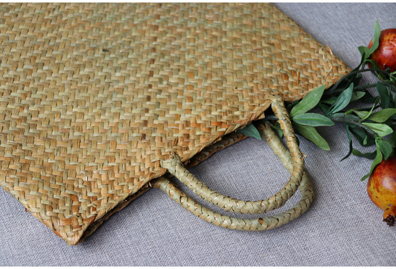 Woven straw bag with handles on a textured surface with pomegranates and leaves.