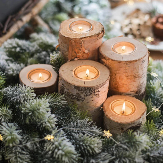 Wooden candle holders with lit candles on a decorative background with greenery and lights.