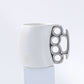 White mug with a metallic knuckle duster handle on a light gray background