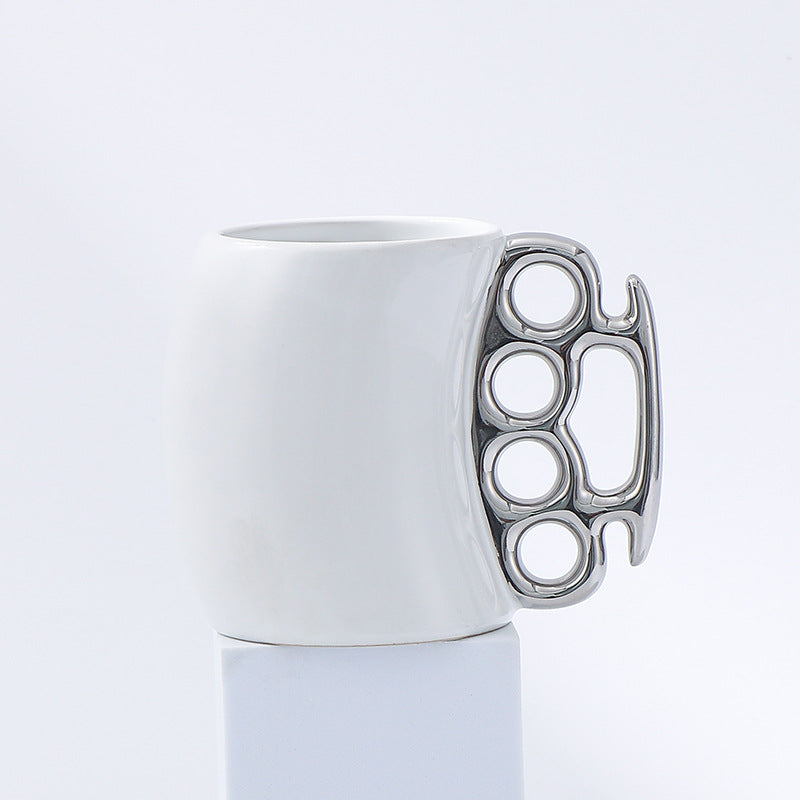 White mug with a metallic knuckle duster handle on a light gray background