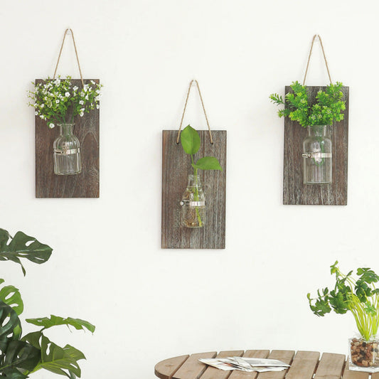 Three wooden wall hangings with glass bottles and plants on a white background