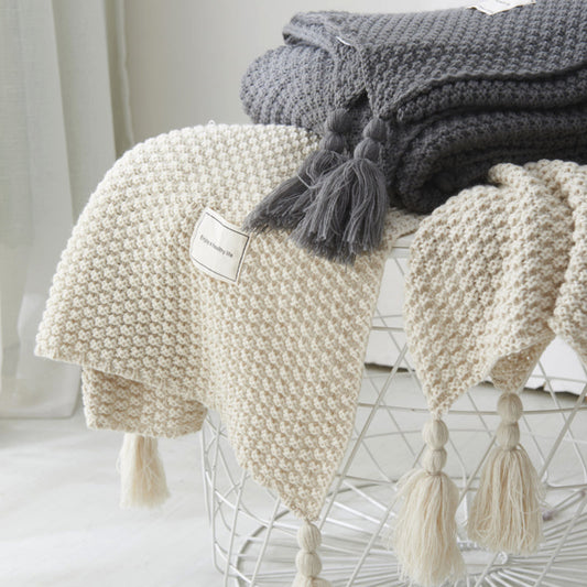 Knitted blankets with tassels on a metal stand against a white background