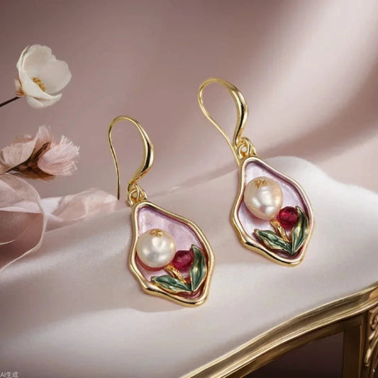 Gold earrings with pearls and red stones on a soft pink background