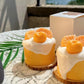 Two small desserts with white cream and orange elements on a textured surface.