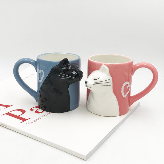 Two cat-shaped mugs, one blue and one pink, on a white surface with a magazine underneath.