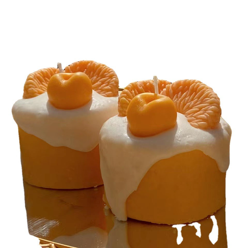 Two orange-themed candles with a white base on a reflective surface.