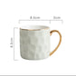 White ceramic mug with gold handle and measurements on a white background