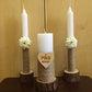 Three candles on wooden stands with floral decorations and a heart-shaped plaque against a beige background.